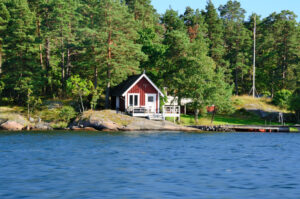 En röd liten stuga med brygga vid en sjö.